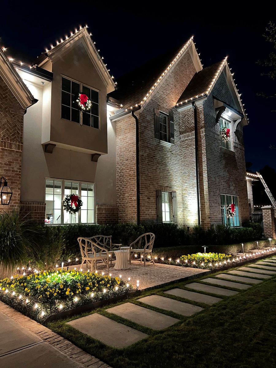 Modern brick home with warm white roofline bulbs, window wreaths and a lit patio and walkway